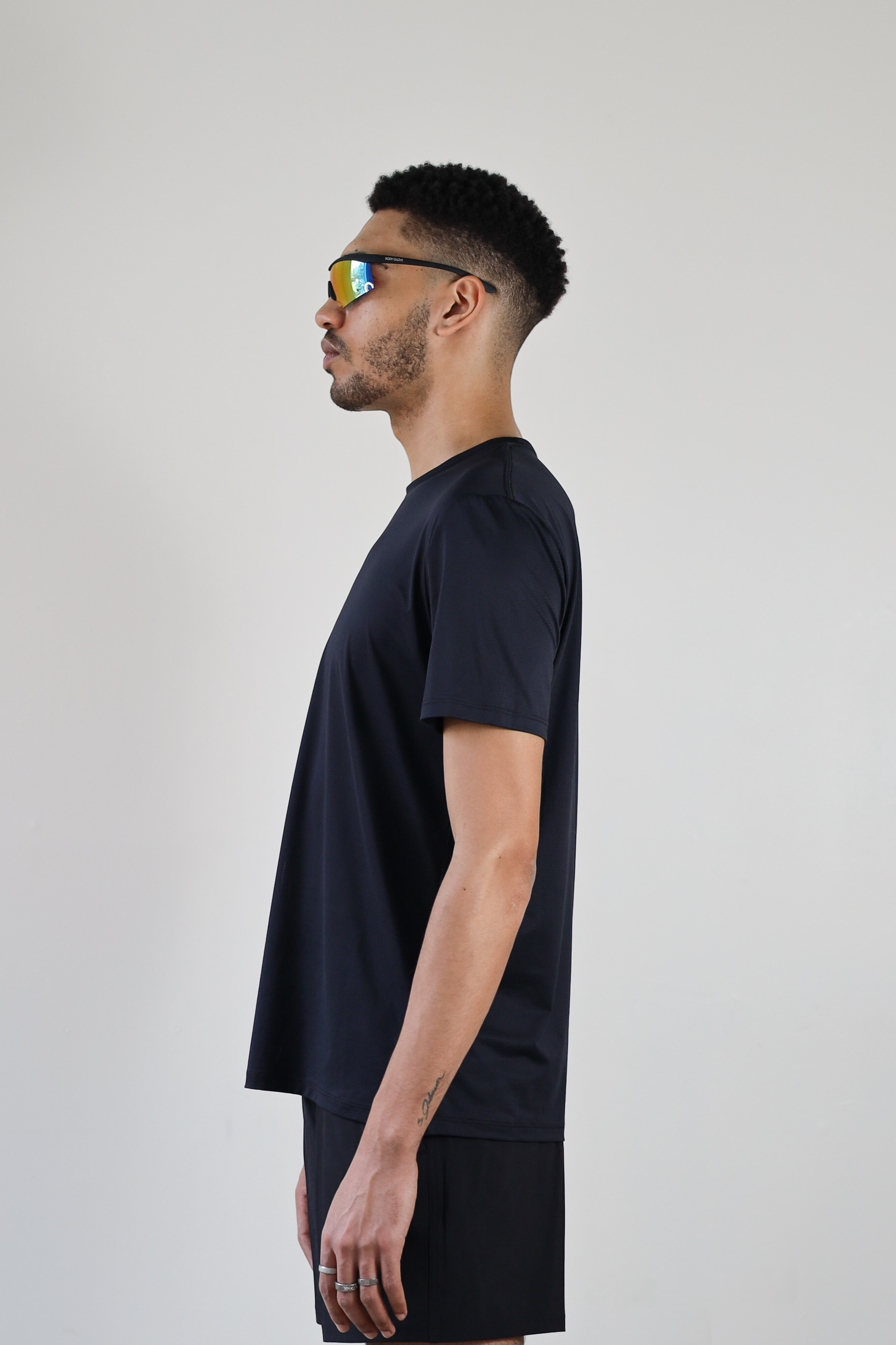 A side view of a model wearing the black Unisex Short Sleeve Runners Tee, emphasizing the ventilated mesh fabric, ergonomic fit, and stretch for unrestricted movement.