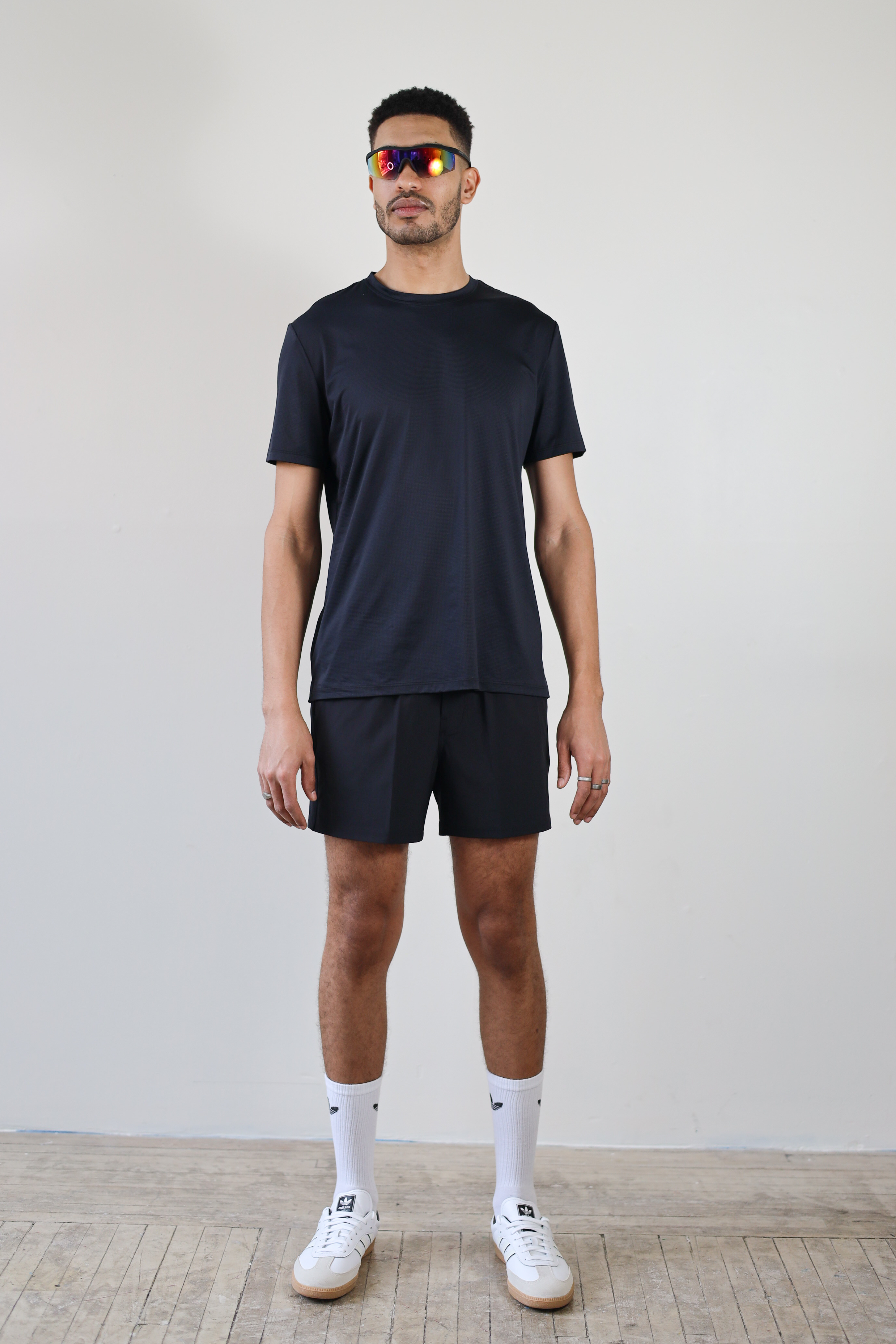 A full-body shot of a model wearing the Unisex Short Sleeve Runners Tee in black, standing front-facing, highlighting its versatile design, breathable fabric, and functional fit for running, training, and everyday wear.