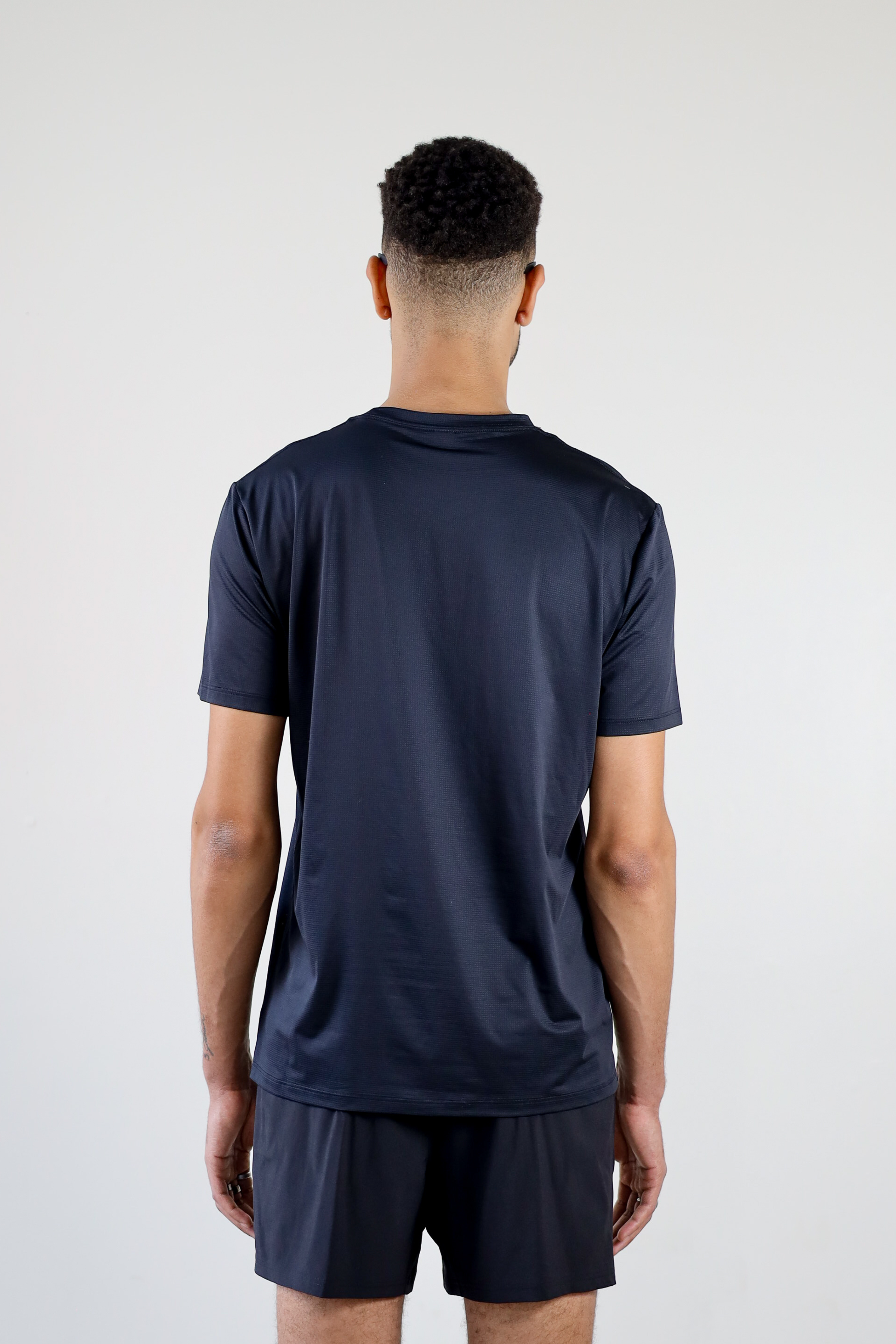  rear view of a model in the black Unisex Short Sleeve Runners Tee, showcasing the minimalist back design, high-performance mesh material, and comfortable, streamlined cut.